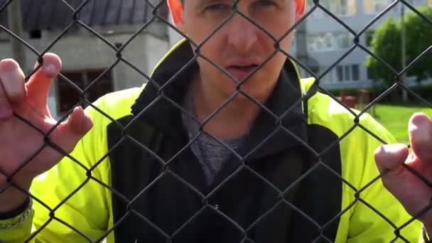 Un homme dans la vingtaine, appuyé contre la clôture regardant la caméra 