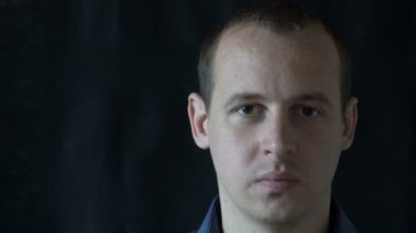 Siyah arka planda, kameraya bakan genç bir adamın portresi.