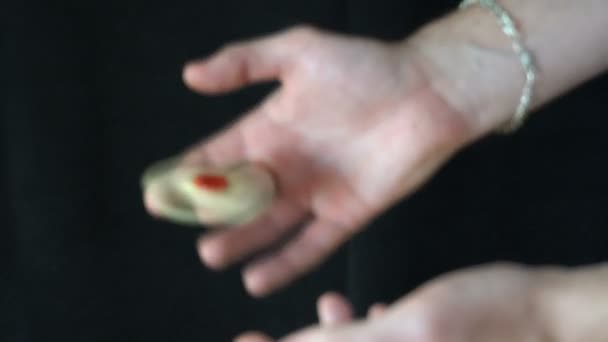 Der Trick mit dem Handspinner auf schwarzem Hintergrund, der junge Mann wirft den Spinner mit einer Hand in die andere — Stockvideo