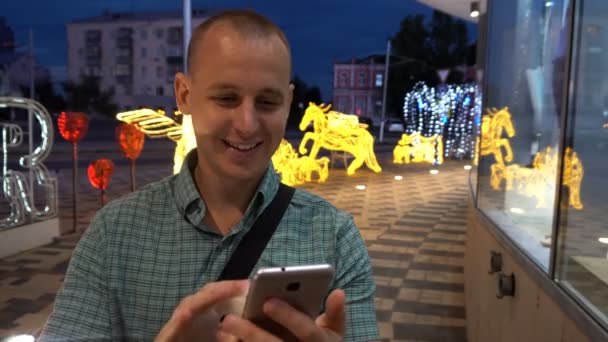 Hombre SMS mensajes de texto utilizando la aplicación en el teléfono inteligente por la noche en la ciudad. Hombre de negocios joven guapo usando teléfono inteligente sonriendo feliz usando camisa de traje al aire libre. Hombre urbano profesional en sus 20 años — Vídeos de Stock