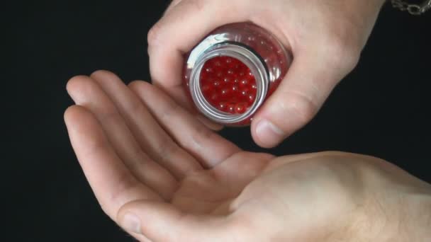 A young man pours it on the palm of his little red round pellets for strike ball weapons — Stock Video