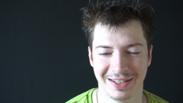 Smiling young man with tousled hair on black background — Stock Video