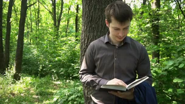 Молодий бізнесмен читає книгу в лісі біля дерева — стокове відео