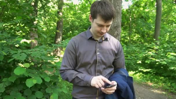 Un jeune homme se tient dans les bois, pense à quelque chose et travaille au téléphone — Video