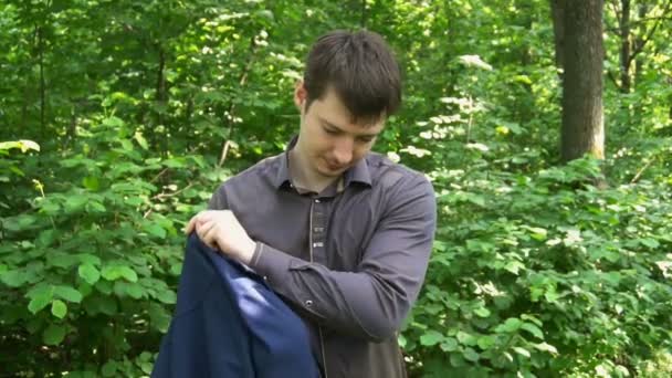 Fiatal üzletember dzsekiben áll az erdőben — Stock videók