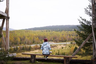  Bir bankın ucunda oturan kız orman manzarasının tadını çıkarıyor. Yüksek kalite fotoğraf
