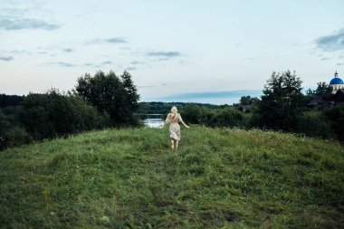 Bir kız yemyeşil bir tarla boyunca gölete koşuyor.