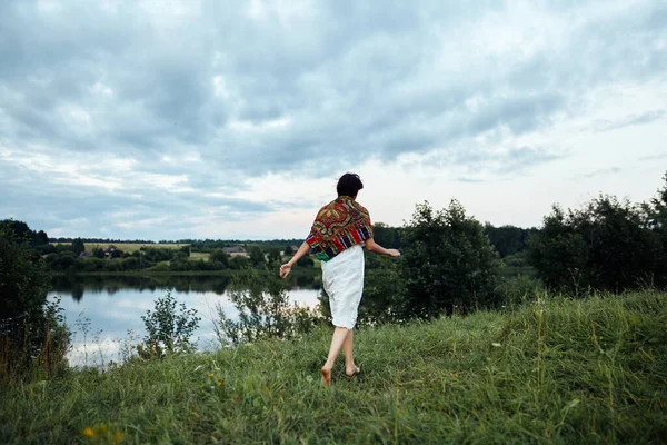 Una ragazza corre lungo un lussureggiante campo verde verso uno stagno — Foto Stock