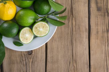 limon ve limes ahşap arka plan üzerinde beyaz bir tabakta yaprakları ile