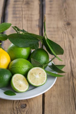 limon ve limes ahşap arka plan üzerinde beyaz bir tabakta yaprakları ile