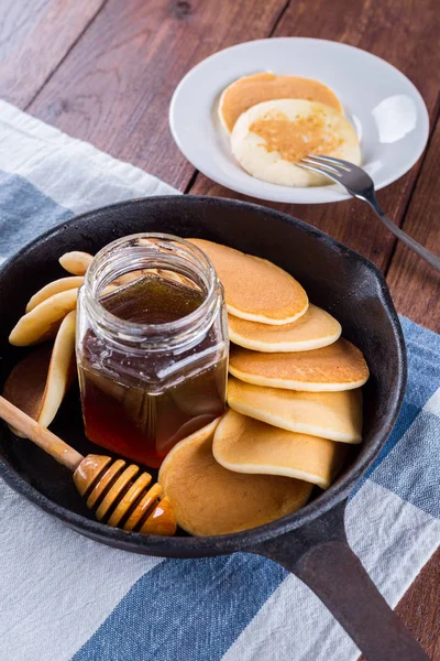 pancakes in a frying pan, honey, wooden background, white tablecloth