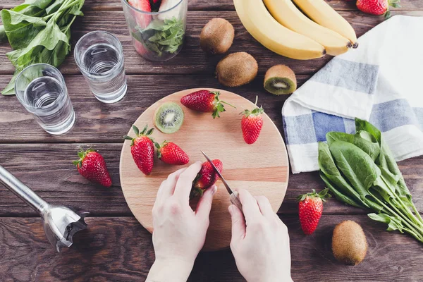 The process of making smoothies from spinach, banana, kiwi and strawberries.