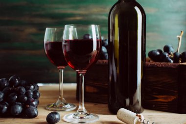 Kırmızı şarap, iki bardak ve koyu yeşil arka planda bir şişe.