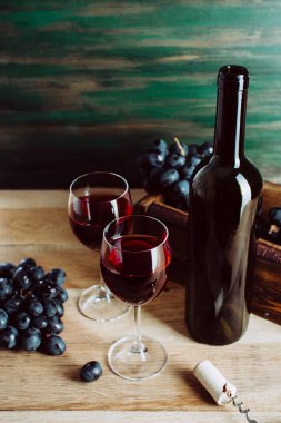 Kırmızı şarap, iki bardak ve koyu yeşil arka planda bir şişe.