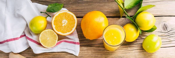 Свежие лимоны и апельсины с зелеными листьями на деревянном фоне, цитрусовый сок и соковыжималка, длинный баннер — стоковое фото
