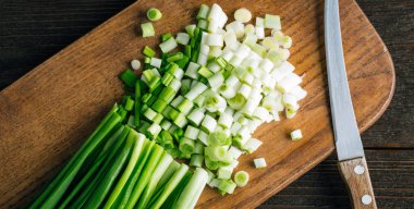 Tahta kesme tahtasının üzerinde dilimlenmiş taze yeşil soğanlar.