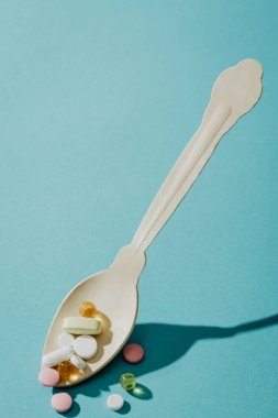 Mavi arka planda kaşıkta farklı haplar, tıbbi geçmiş.