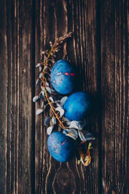 Üç mavi paskalya yumurtası ve koyu ahşap arka planda çiçek.