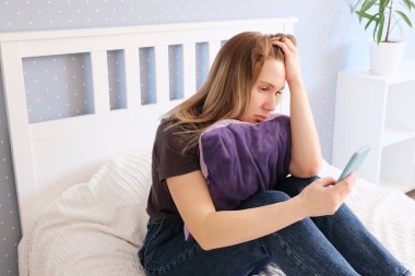 Güzel bir kadın elinde akıllı bir telefonla yatakta poz veriyor.