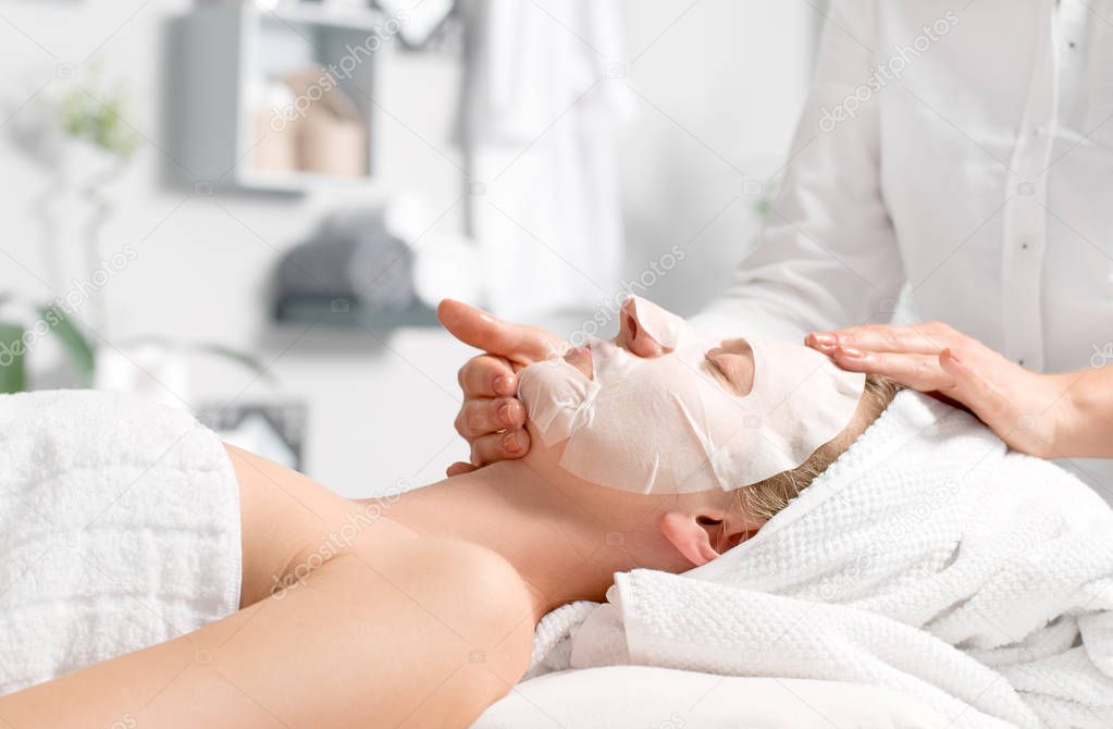 Beautiful young woman is getting facial mask at spa