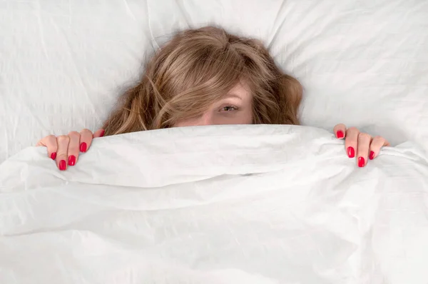 Αστεία νεαρή όμορφη γυναίκα ξαπλωμένη στο κρεβάτι κάτω από την κουβέρτα — Φωτογραφία Αρχείου
