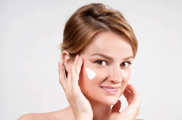 Il concetto di bellezza e cura della pelle. Giovane donna che applica crema idratante sul viso . — Foto Stock