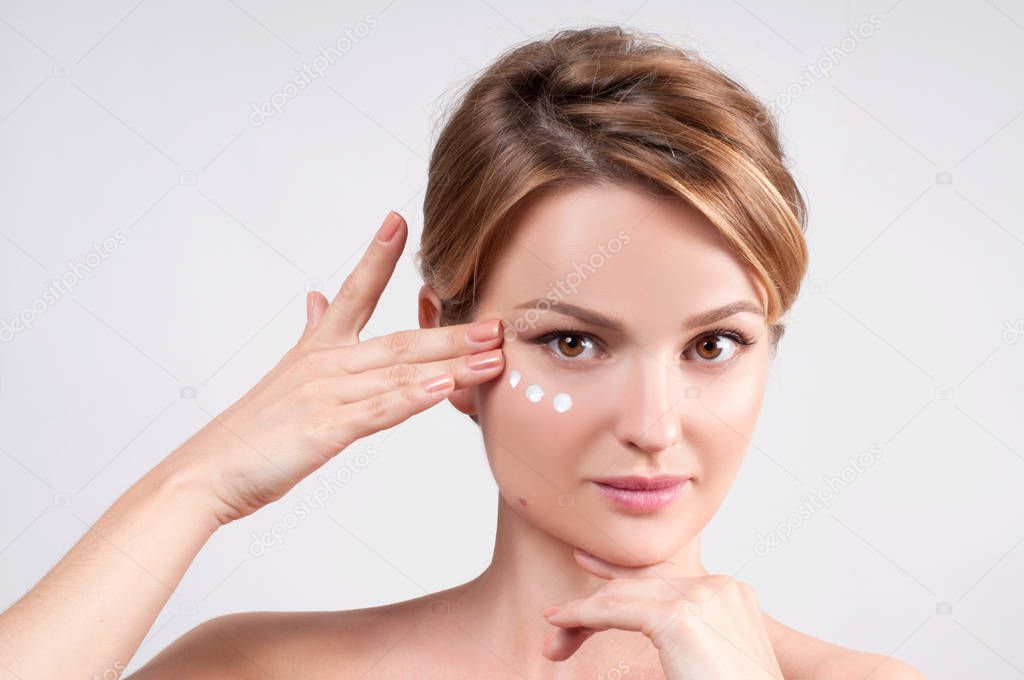 Beauty and skincare concept. Young woman applying moisturizer on face.