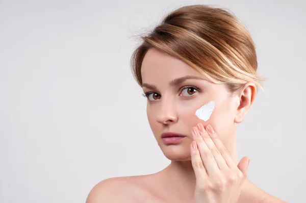 Concepto de belleza y cuidado de la piel. Mujer joven aplicando crema hidratante en la cara . —  Fotos de Stock