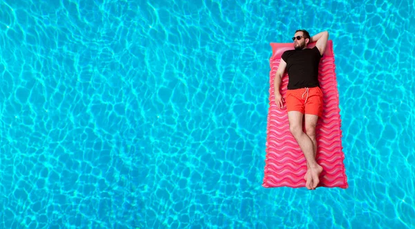 Uomo in t-shirt e pantaloncini su materasso gonfiabile in piscina . — Foto Stock