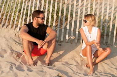 Genç güzel çift sahilde oturup gün batımı ve romantik bir atmosfer keyfini çıkarın.. 