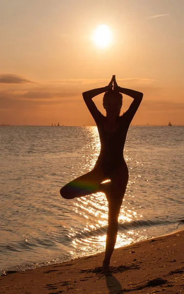 Silhouette einer jungen Frau, die bei Sonnenuntergang Yoga am Meer praktiziert — Stockfoto