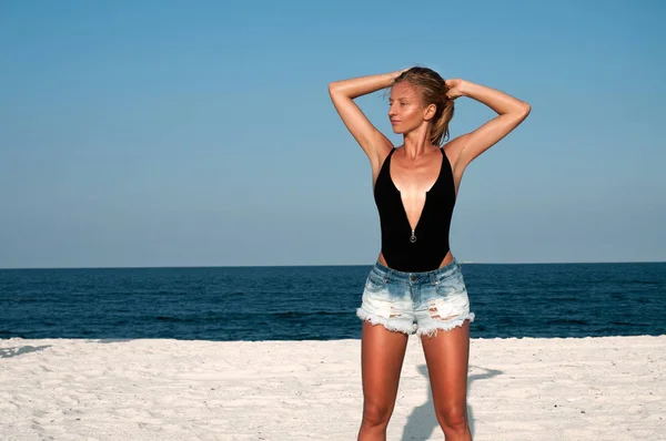 Красивая женщина в черном купальнике и джинсовых шортах на пляже . — стоковое фото