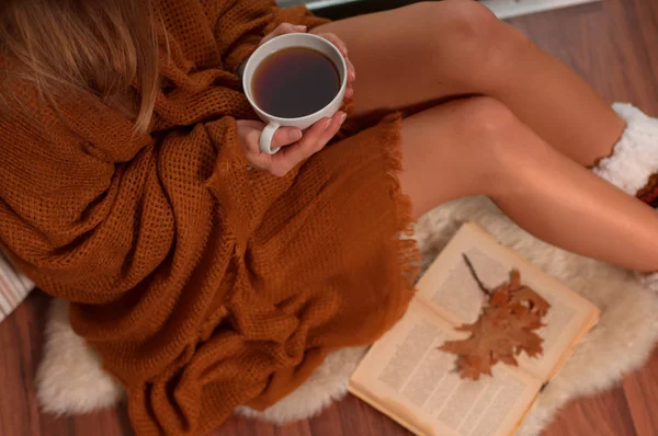Donna avvolta in una calda coperta a quadri bere tè caldo e leggere un libro in autunno — Foto Stock