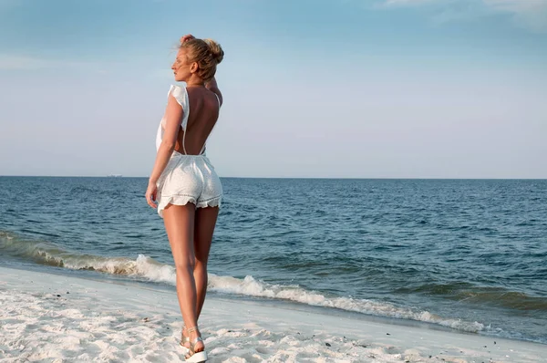 Menina em vestido de verão em pé em uma praia e olhando para o mar — Fotografia de Stock
