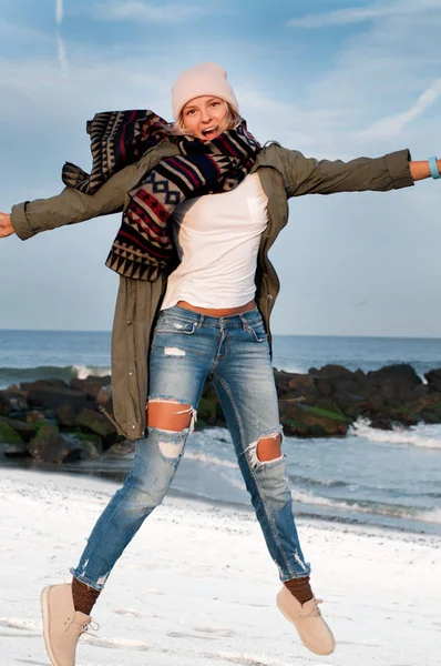 Femeia fericită în jachete și șapcă caldă sărind pe plajă toamna — Fotografie, imagine de stoc