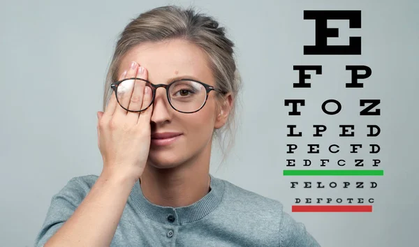 Kvinna på bakgrunden av ögat test diagram, eye care koncept — Stockfoto