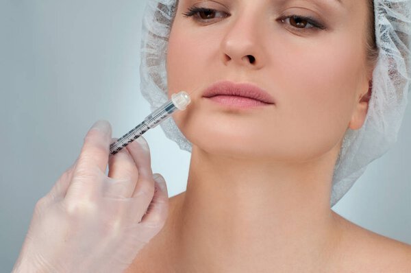 Beautiful girl receiving filler injection in lips. Plastic Surgery.