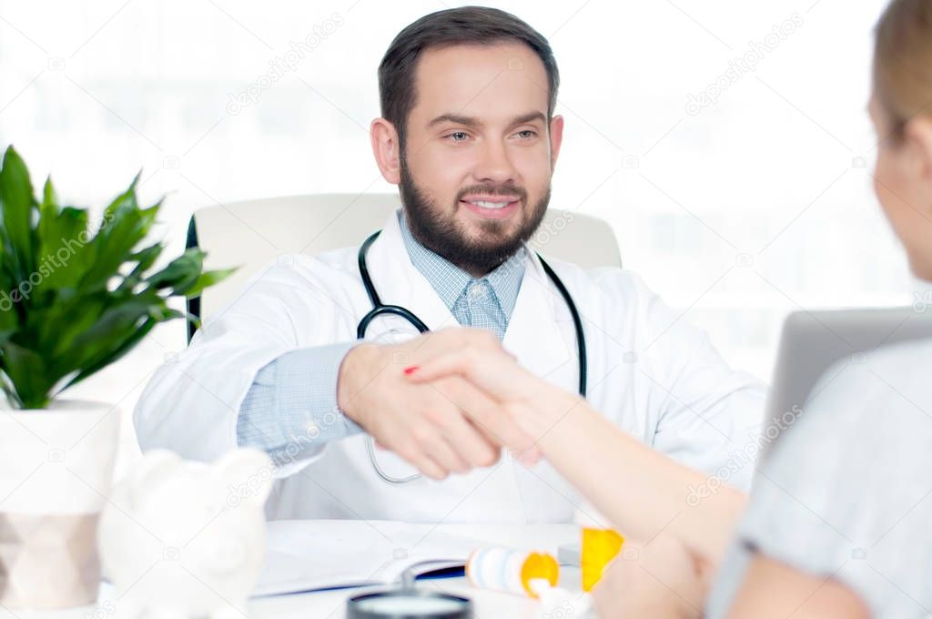 Smiling doctor shaking hands with a female patient in the office