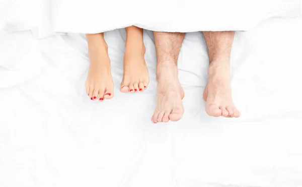 Close up van de voeten van een paar op het bed. — Stockfoto