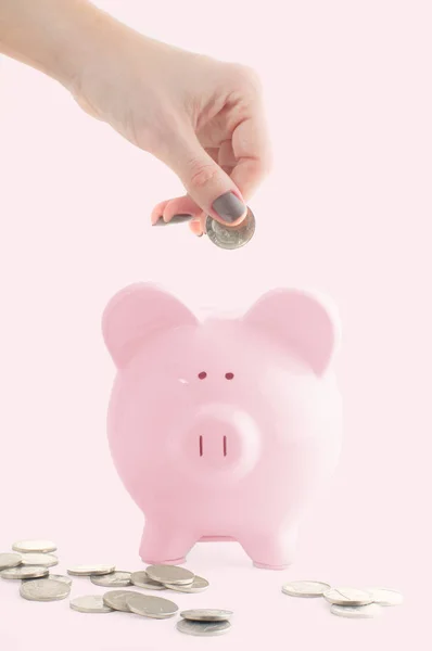 女性手放硬币到小猪银行在粉彩粉红色背景 — 图库照片