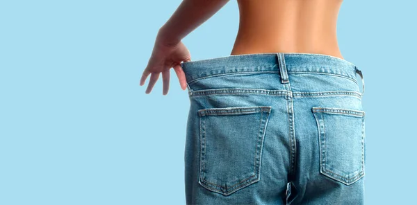 Женщина в огромных джинсах после потери веса на голубом фоне — стоковое фото
