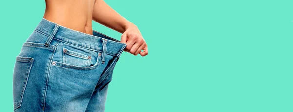 Perda de peso. Mulher em jeans de tamanho grande em fundo verde — Fotografia de Stock