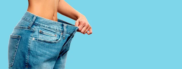 Потеря веса. Женщина в огромных джинсах на синем фоне — стоковое фото