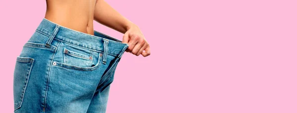 Weight loss. Woman in oversize jeans on pink background — Stock Photo, Image