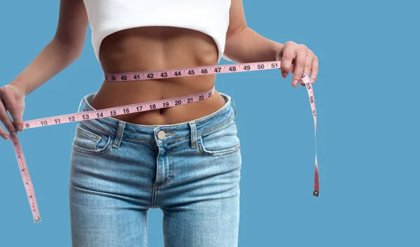 Mujer está midiendo la cintura después de la pérdida de peso en el fondo azul pastel — Foto de Stock