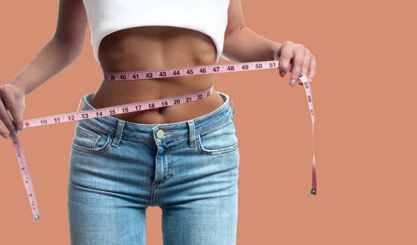 Woman is measuring waist after weight loss on pastel background — Stock Photo, Image
