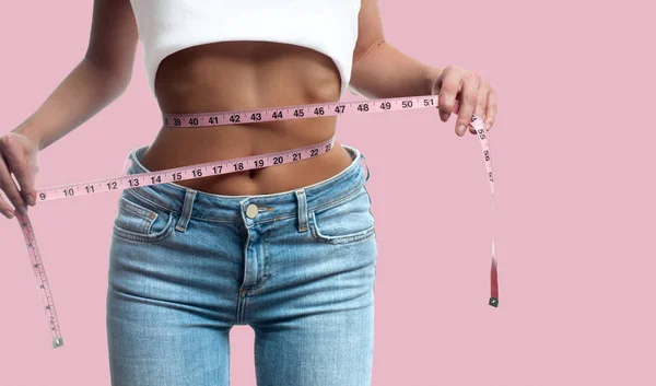 Woman is measuring waist after weight loss on pastel pink backgr — Stock Photo, Image