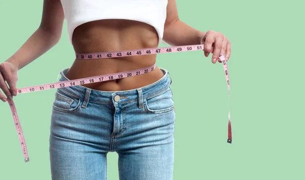Woman is measuring waist after weight loss on pastel green backg — Stock Photo, Image