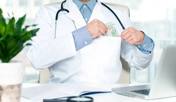 Doctor poniendo un billete de cien dólares en su bolsillo —  Fotos de Stock