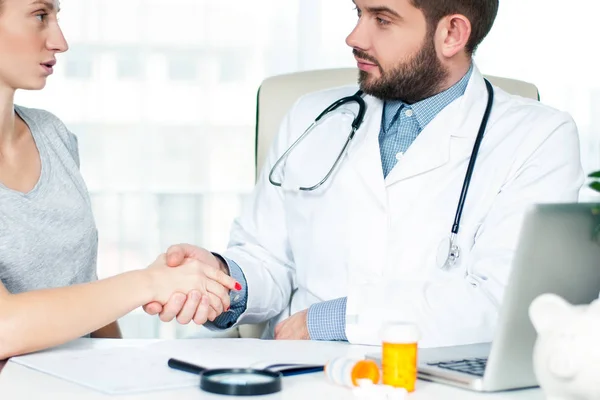 Улыбающийся доктор пожимает руку пациентке в офисе — стоковое фото